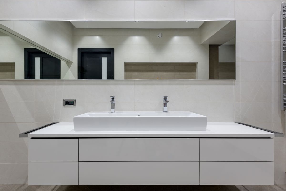 A minimalist bathroom with a white vanity unit and a wide mirror