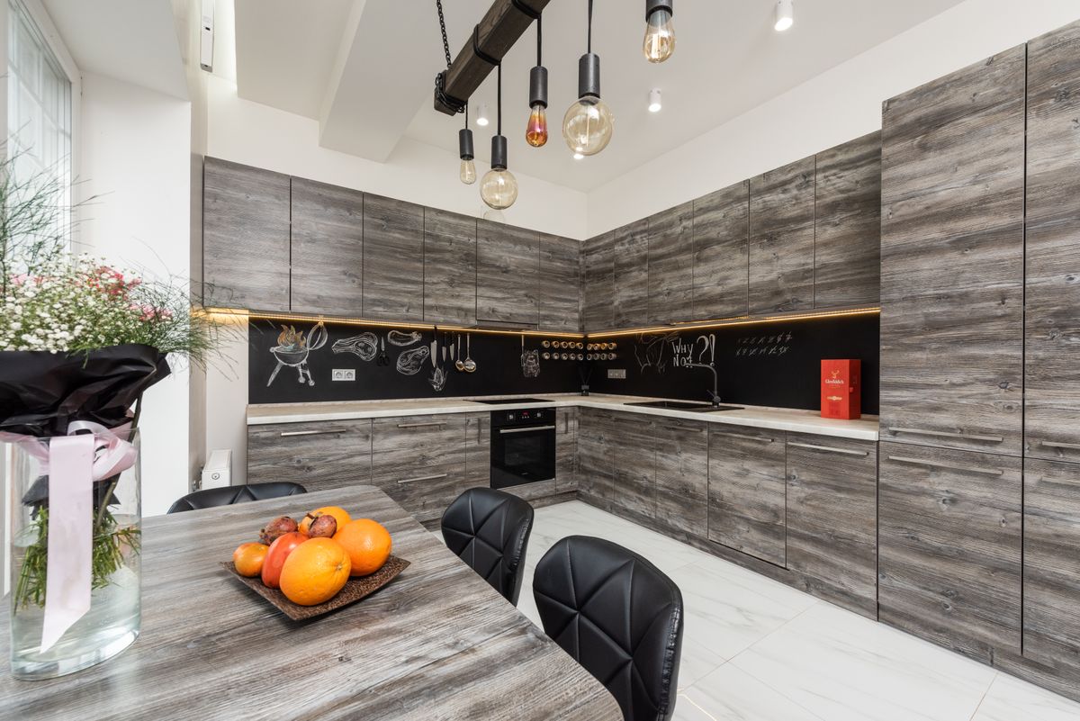 A grey wood-grain kitchen with a dining table and pendant lights